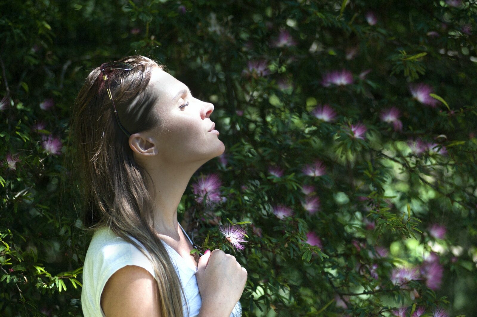 Woman Closing Her Eyes Against Sun Light Standing Near Purple Petaled Flower Plant