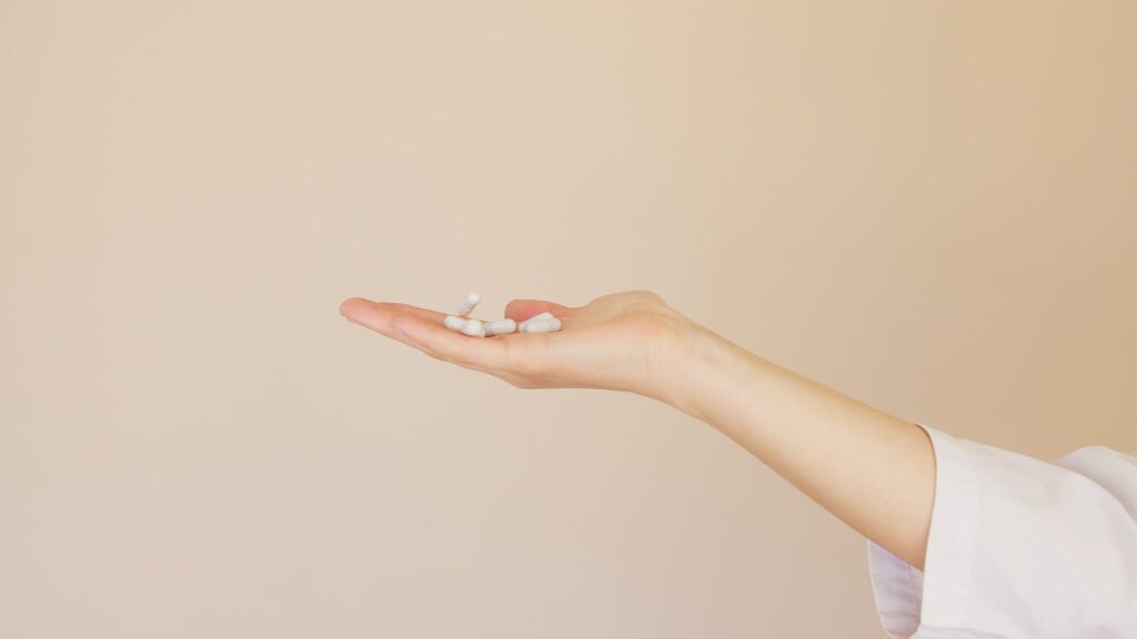 A female hand in a lab coat holds white capsules against a neutral background.