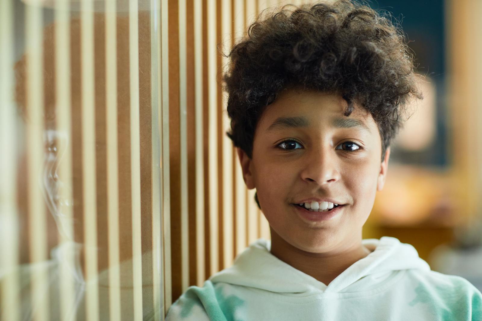 Close-up portrait of a young boy smiling warmly indoors with a blurred background.