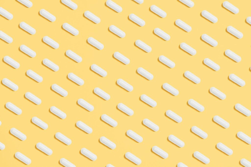 Pattern of white capsules on a bright yellow surface, symbolizing healthcare and medicine.