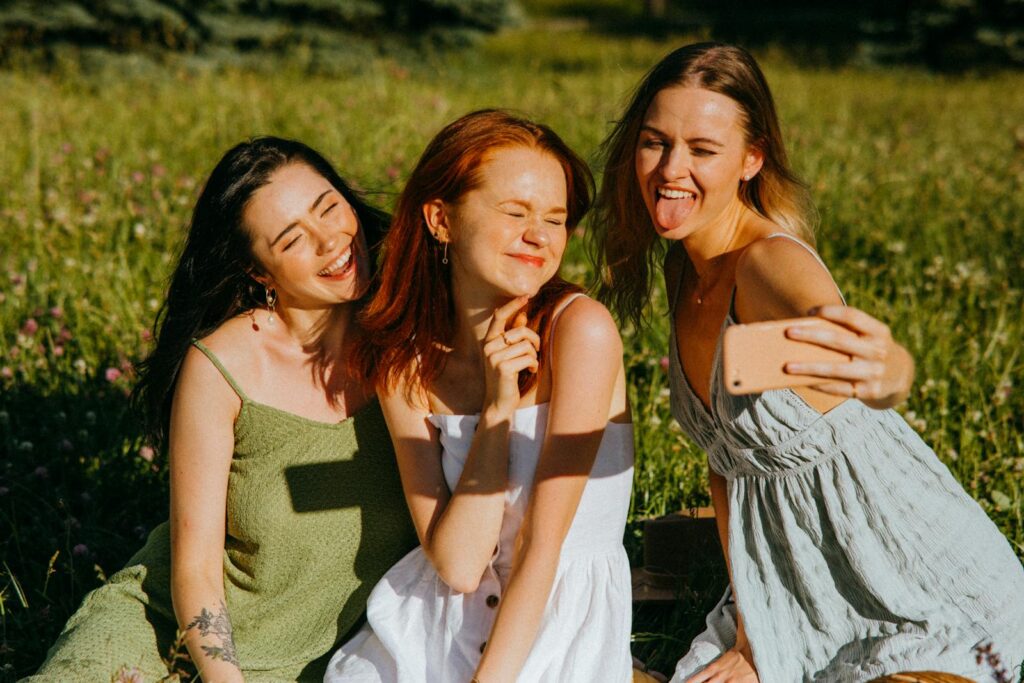 Three young women enjoying a cheerful selfie outdoors in a sunny park, capturing fun and friendship.