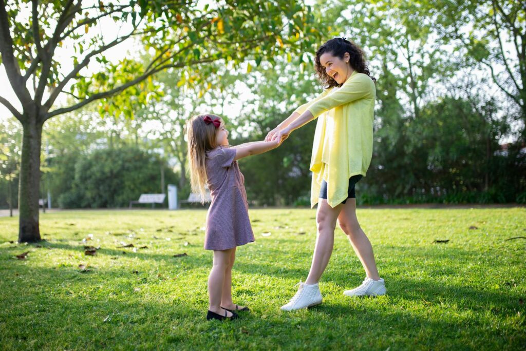 Mother and daughter enjoying a playful moment in a sunny park, holding hands and smiling.