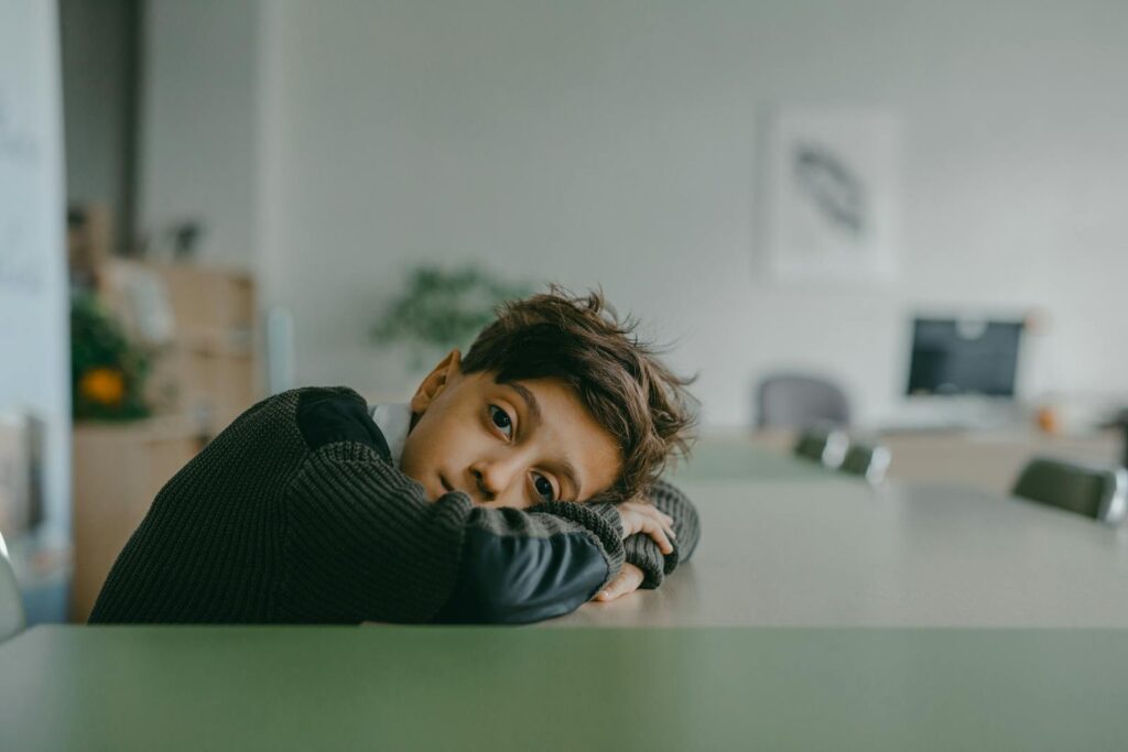 A contemplative child rests on a desk in a quiet classroom setting.